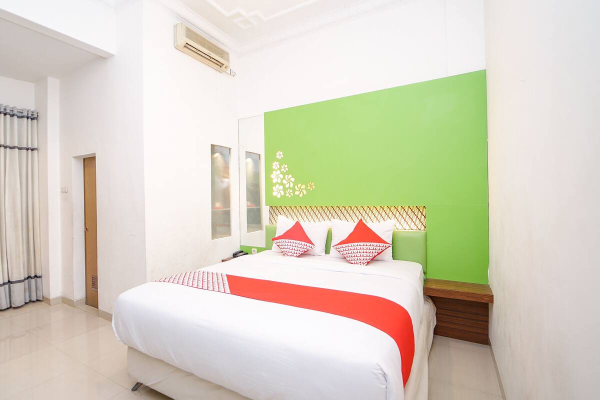 A hotel room with a bed, a green accent wall, and a window.