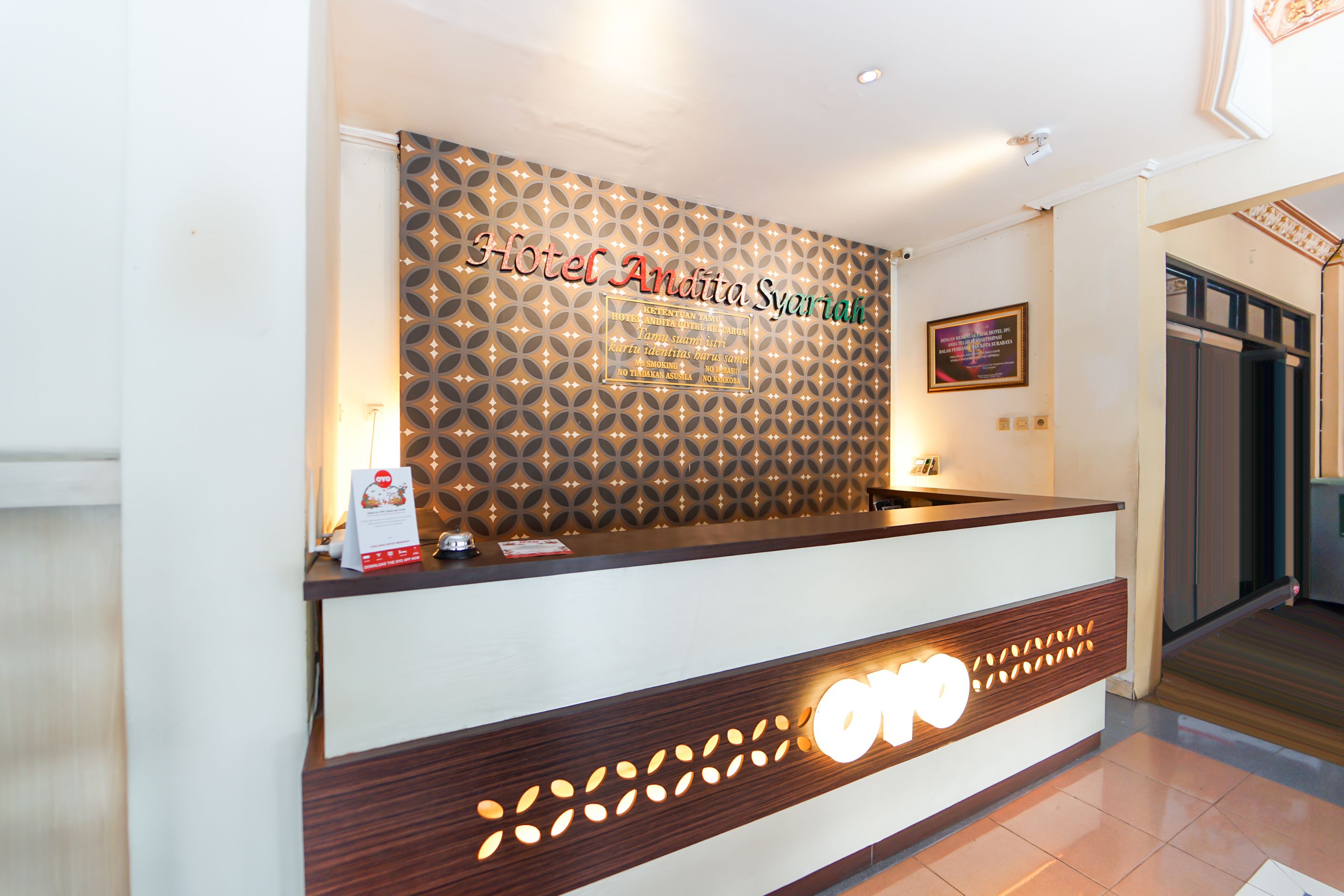 A hotel reception desk with a patterned wall and a sign that reads "Hotel Andia Syariah."