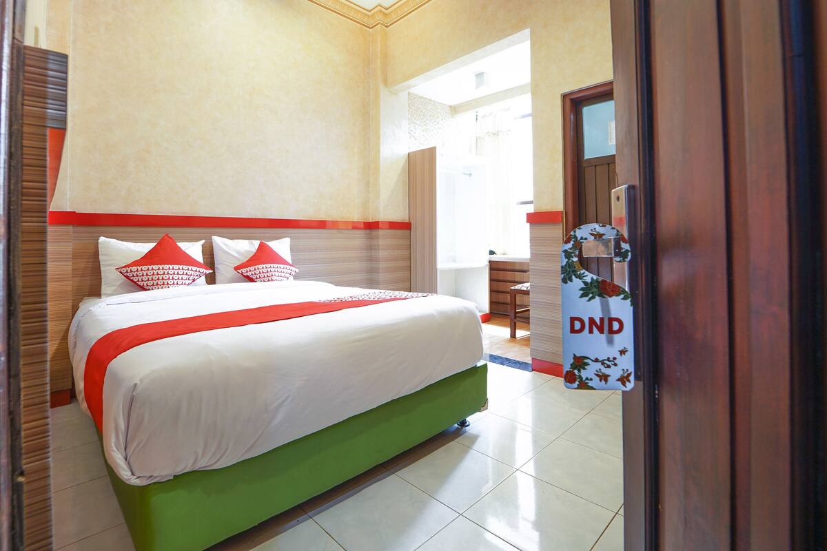 A hotel room with a bed, a green upholstered headboard, and a door with a sign that reads "DND".