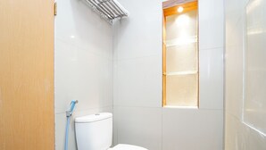 Une petite salle de bain avec des toilettes blanches, un espace douche et une fenêtre.