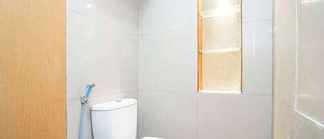A small bathroom with a white toilet, a shower area, and a window.