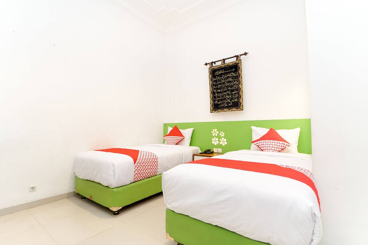 A hotel room with two beds, each with green and white bedding, and a wall-mounted blackboard with Arabic writing.