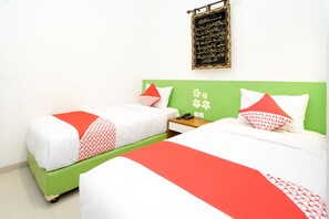 Two single beds with green and white bedding, a small bedside table with a phone, and a wall-mounted decorative item.