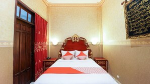 Une chambre d’hôtel avec un grand lit, des rideaux rouges, une porte en bois et un mur orné de calligraphies arabes.