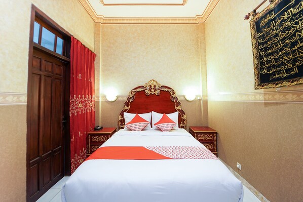 A hotel room with a large bed, red curtains, a wooden door, and a wall with Arabic calligraphy.