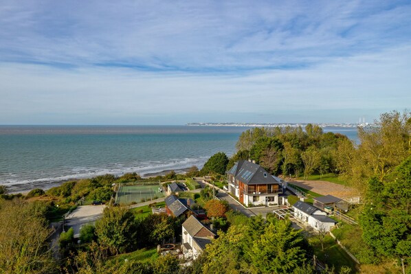 A coastal residential area with houses, a tennis court, and a view of the sea.