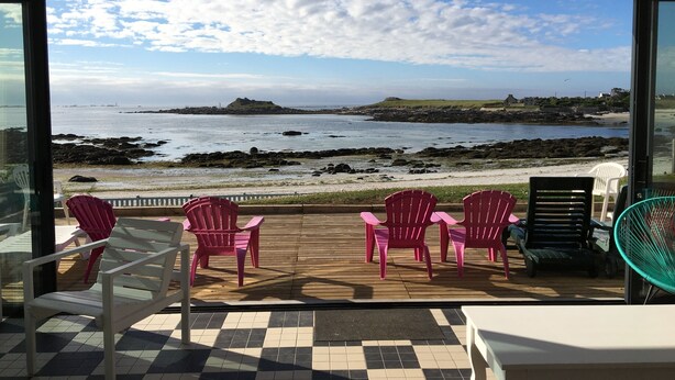 Varanda com vista para o mar, com chão quadriculado, mesa branca e várias cadeiras.