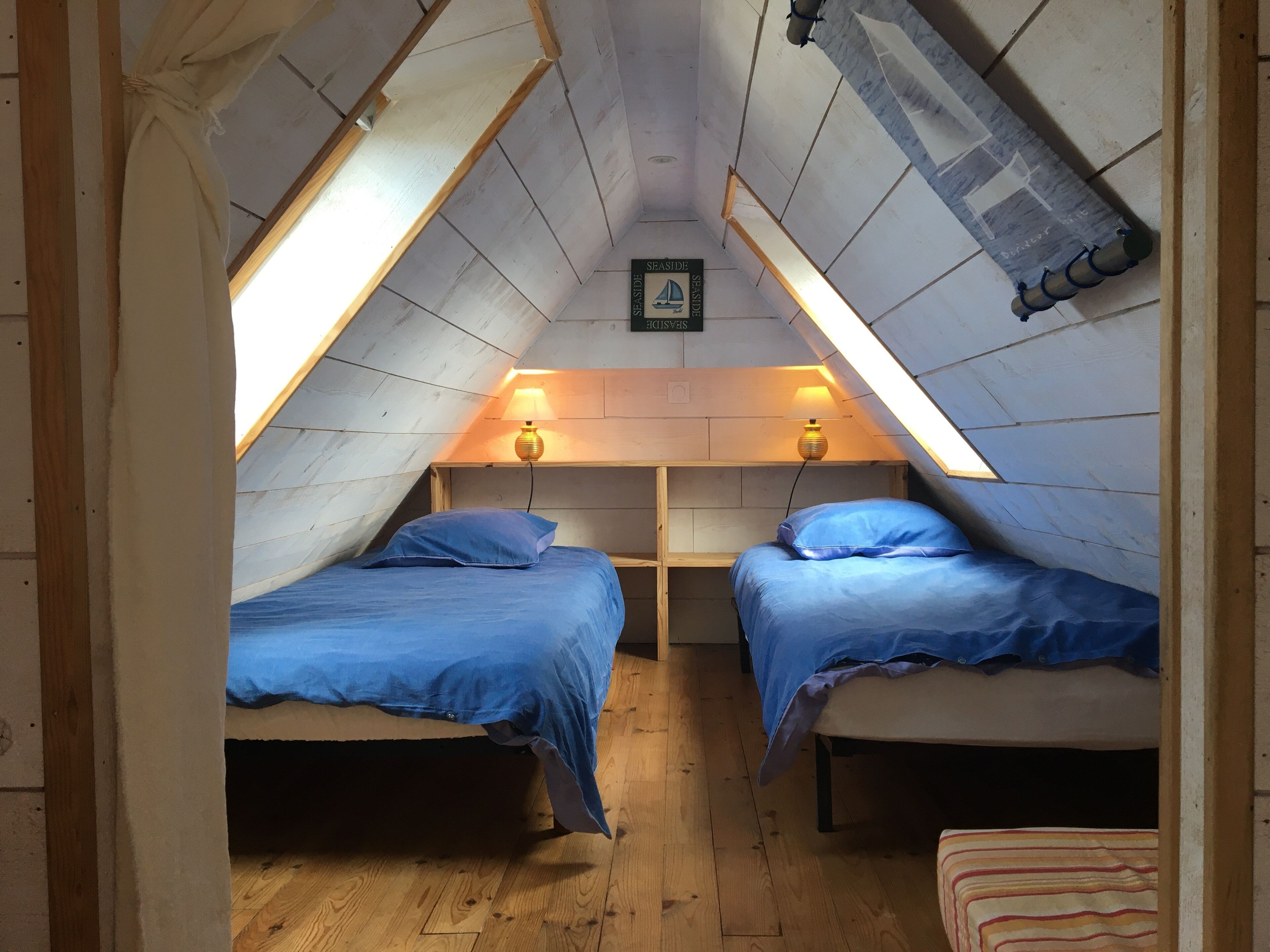 Un pequeño dormitorio en el ático con dos camas, paredes de madera y techo inclinado.