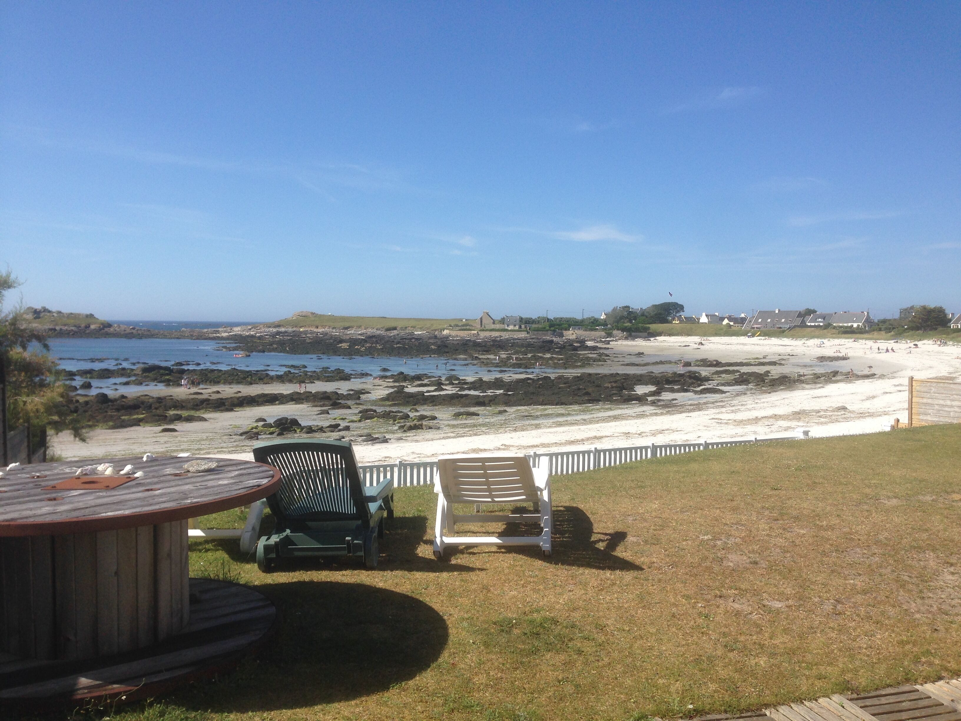 A patio with two lawn chairs and a table, overlooking a rocky beach and a clear blue sky.