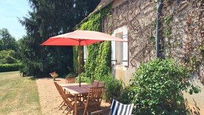 Une terrasse avec une table et des chaises, un parasol rouge et un mur de pierre recouvert de lierre.