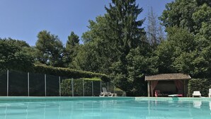 Une piscine aux eaux cristallines, dotée de chaises longues et d’un petit pavillon, située dans un espace boisé.