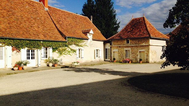 Un bâtiment traditionnel en pierre, doté d’un toit en tuiles, entouré d’une cour pavée de gravier.