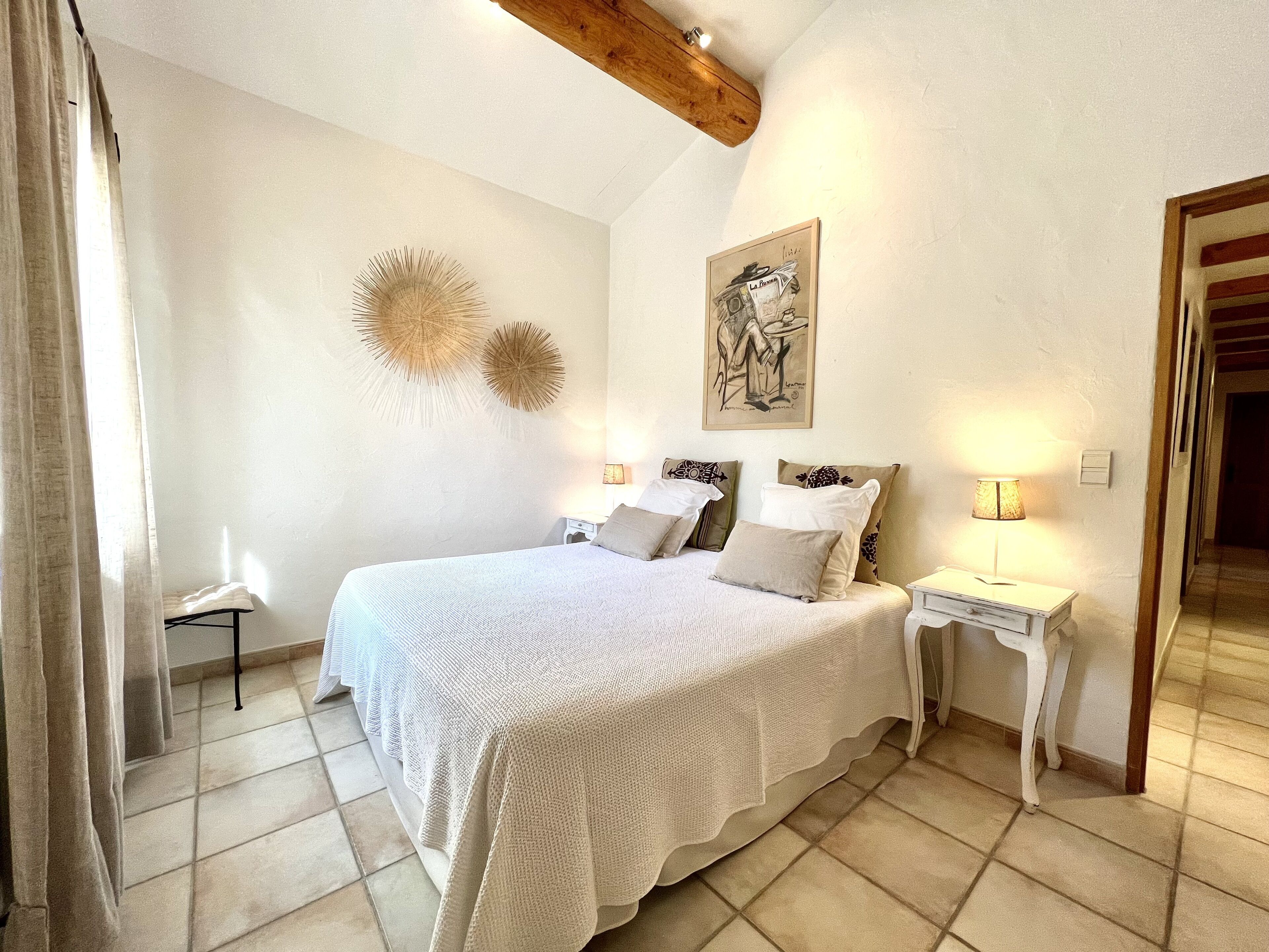 A bedroom with a large bed, two wall-mounted lamps, a small bedside table, and a door leading to another room.