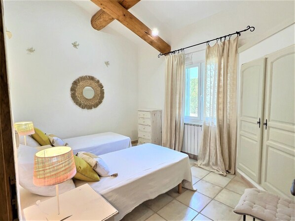 A bedroom with two beds, a dresser, a mirror, and a window with curtains.