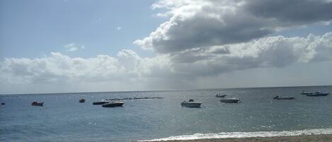 A beach with boats on the water and a cloudy sky.