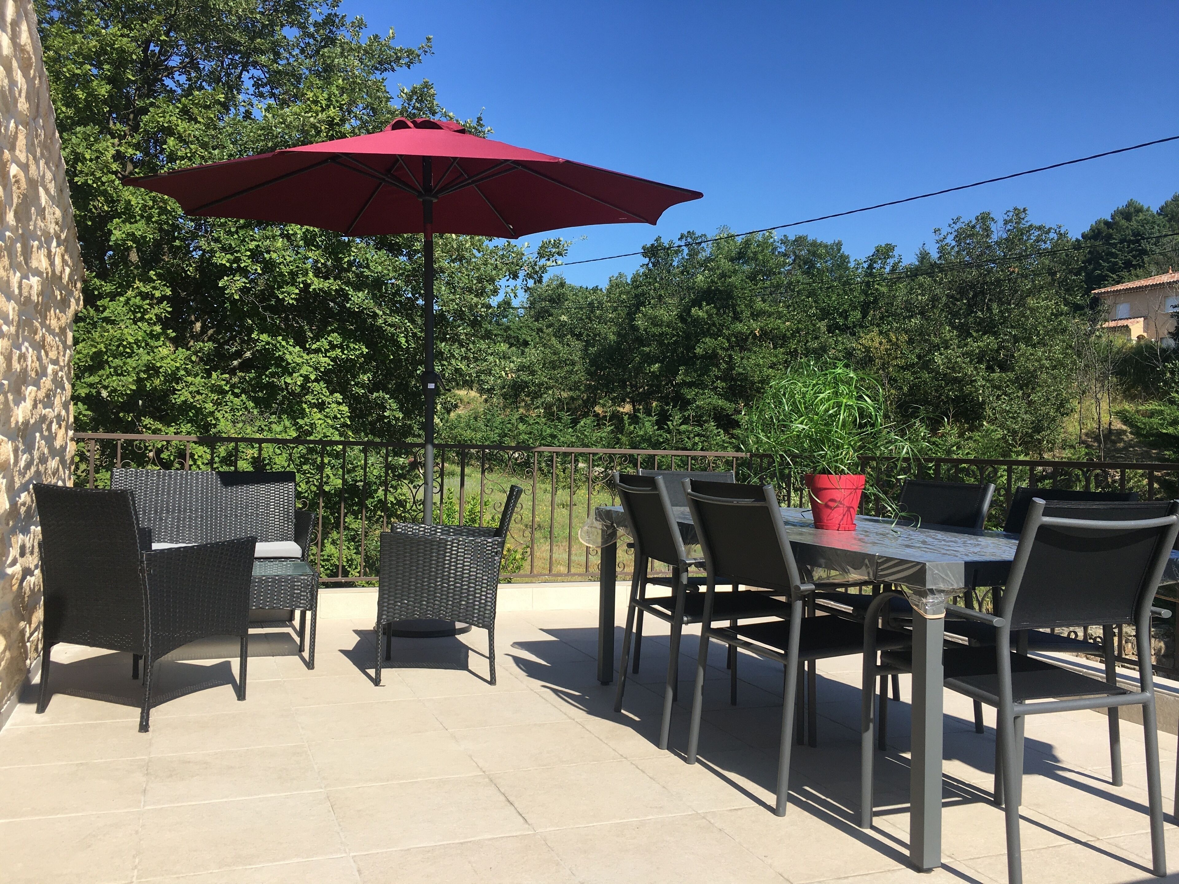 An outdoor patio with a table and chairs, a red umbrella, and a potted plant.