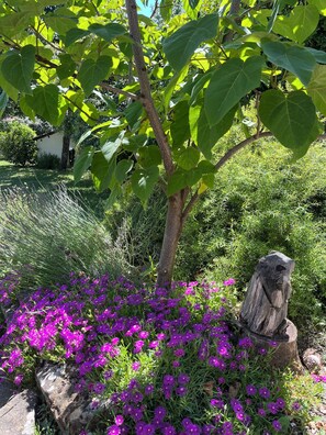 A garden with a tree, purple flowers, and a wooden sculpture.