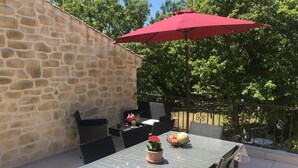 An outdoor patio with a stone wall, a table with chairs, a red umbrella, and potted plants. - Quiet country house with swimming pool, ideal location. (Tauriers)