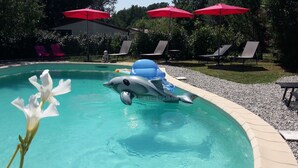 A swimming pool with a dolphin float, lounge chairs, and red umbrellas. - Quiet country house with swimming pool, ideal location. (Tauriers)