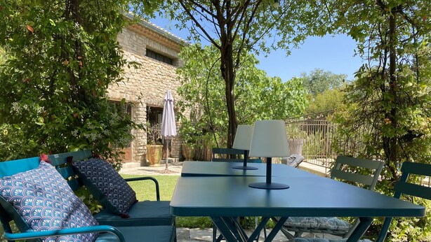 A patio with outdoor furniture, including a table and chairs, set against a stone building with a garden. - Charming apartment in Provencal farmhouse in Saint-Rémy-de-Provence (Saint-Rémy-De-Provence)