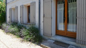 A building with white exterior walls, shuttered windows, and a wooden door with glass panels. - Charming apartment in Provencal farmhouse in Saint-Rémy-de-Provence (Saint-Rémy-De-Provence)