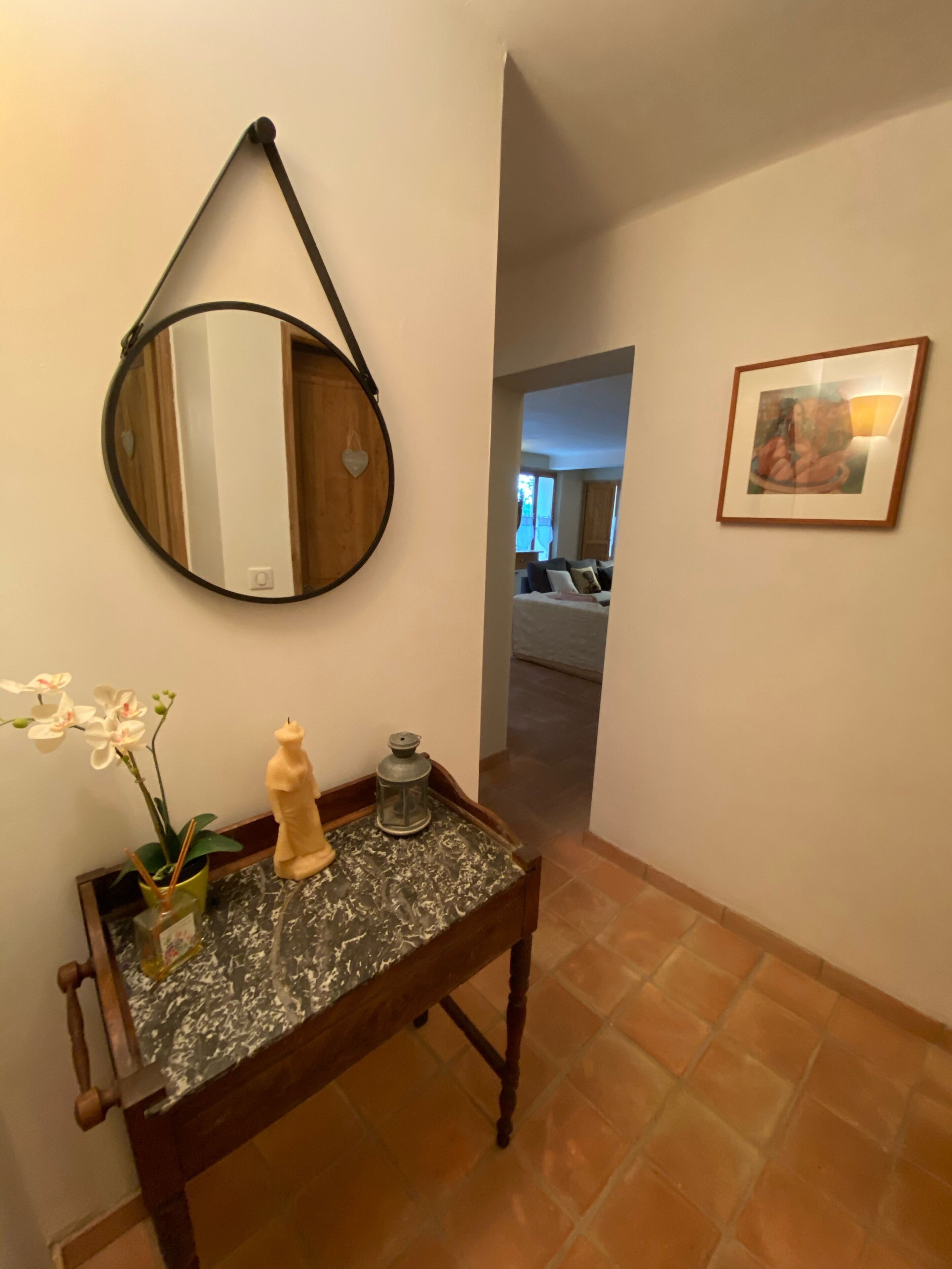 A hallway with a round mirror, a small table with a plant, a decorative lantern, and a framed picture on the wall.