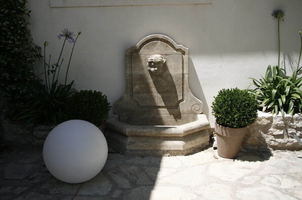 Una escultura de piedra con la cabeza de un león, un objeto blanco esférico y una planta en maceta en un patio.