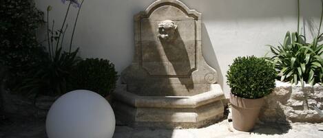 Una escultura de piedra con la cabeza de un león, un objeto blanco esférico y una planta en maceta en un patio.