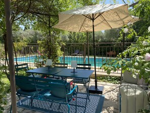 An outdoor seating area with a table and chairs, a large umbrella, and a view of a swimming pool. - Charming apartment in Provencal farmhouse in Saint-Rémy-de-Provence (Saint-Rémy-De-Provence)