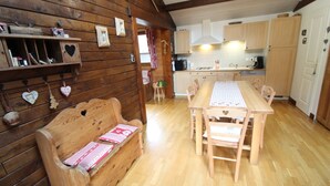 Un interior de madera con una mesa de comedor y bancos, un banco de madera con adornos con forma de corazón y una zona de cocina con armarios y electrodomésticos.