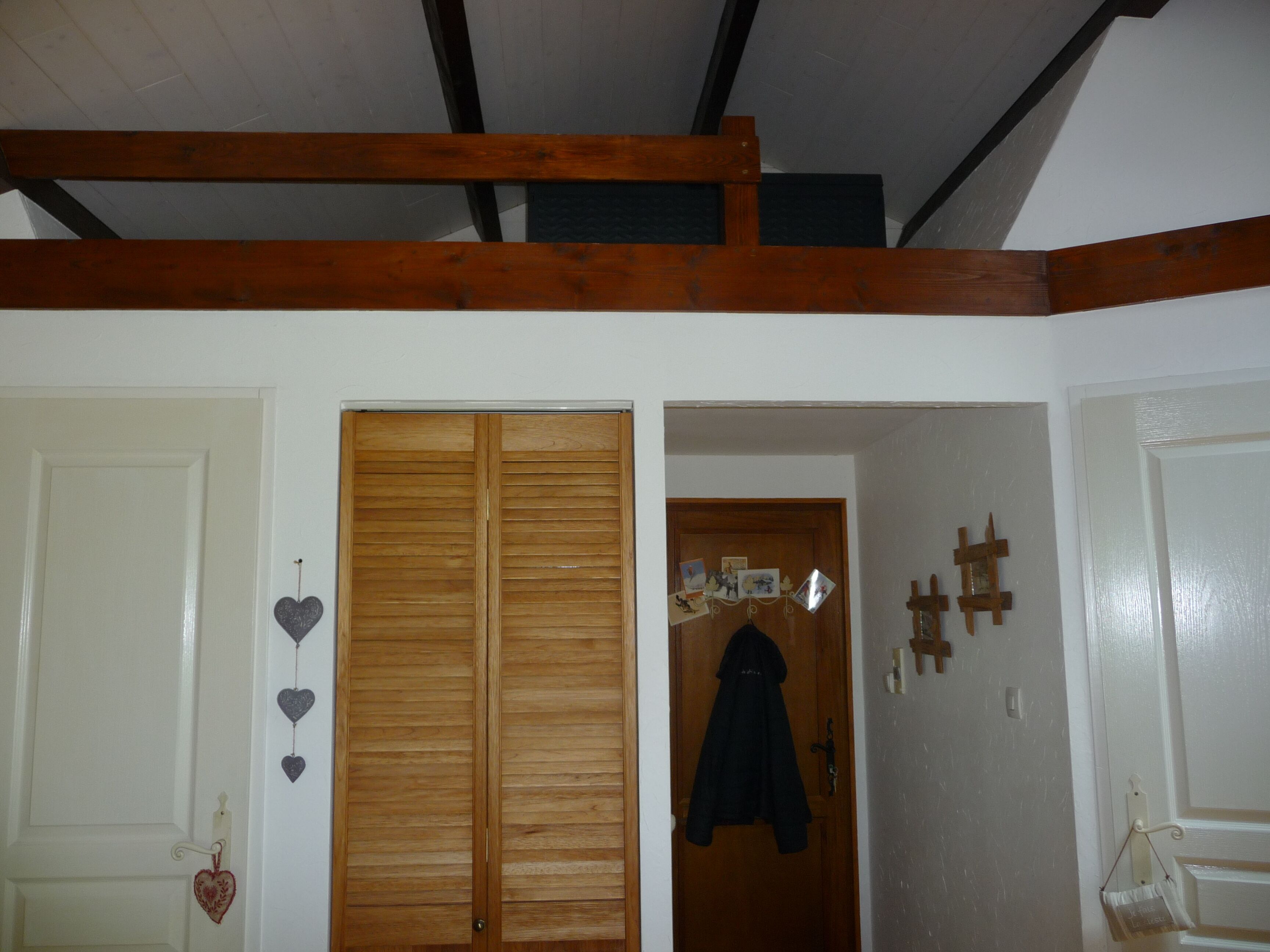 Ein Zimmer mit einer Holztür, einem an der Tür hängenden Mantel und einer Wand mit Kreuz- und Herzdekorationen.