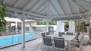 Un espace extérieur abrité comprenant une piscine, une table avec des chaises et un hamac.