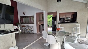 Une cuisine moderne équipée d’un téléviseur, un coin repas avec une table en verre et des chaises blanches, ainsi qu’une petite table d’appoint agrémentée d’un objet décoratif.
