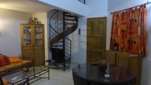 Un vaste espace de vie agrémenté d’un escalier en colimaçon, d’une table basse en verre et d’un canapé avec des coussins.