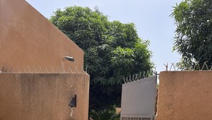 Une entrée fermée par un portail, avec un chemin de gravier menant à un espace ombragé agrémenté de plantes en pot et d’un coin salon.