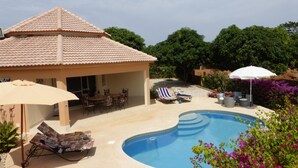 Un espace aménagé au bord de la piscine, comprenant un coin salon couvert, des chaises longues et une piscine.