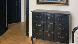 Une pièce avec une commode noire, un grand miroir décoratif et un parquet en bois disposé en motif chevrons.