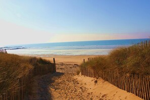 A sandy beach path leading to the ocean, flanked by wooden fences and grass.