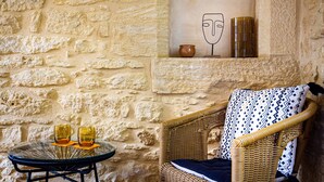 Un muro de piedra, una silla de mimbre y una pequeña mesa con dos vasos.