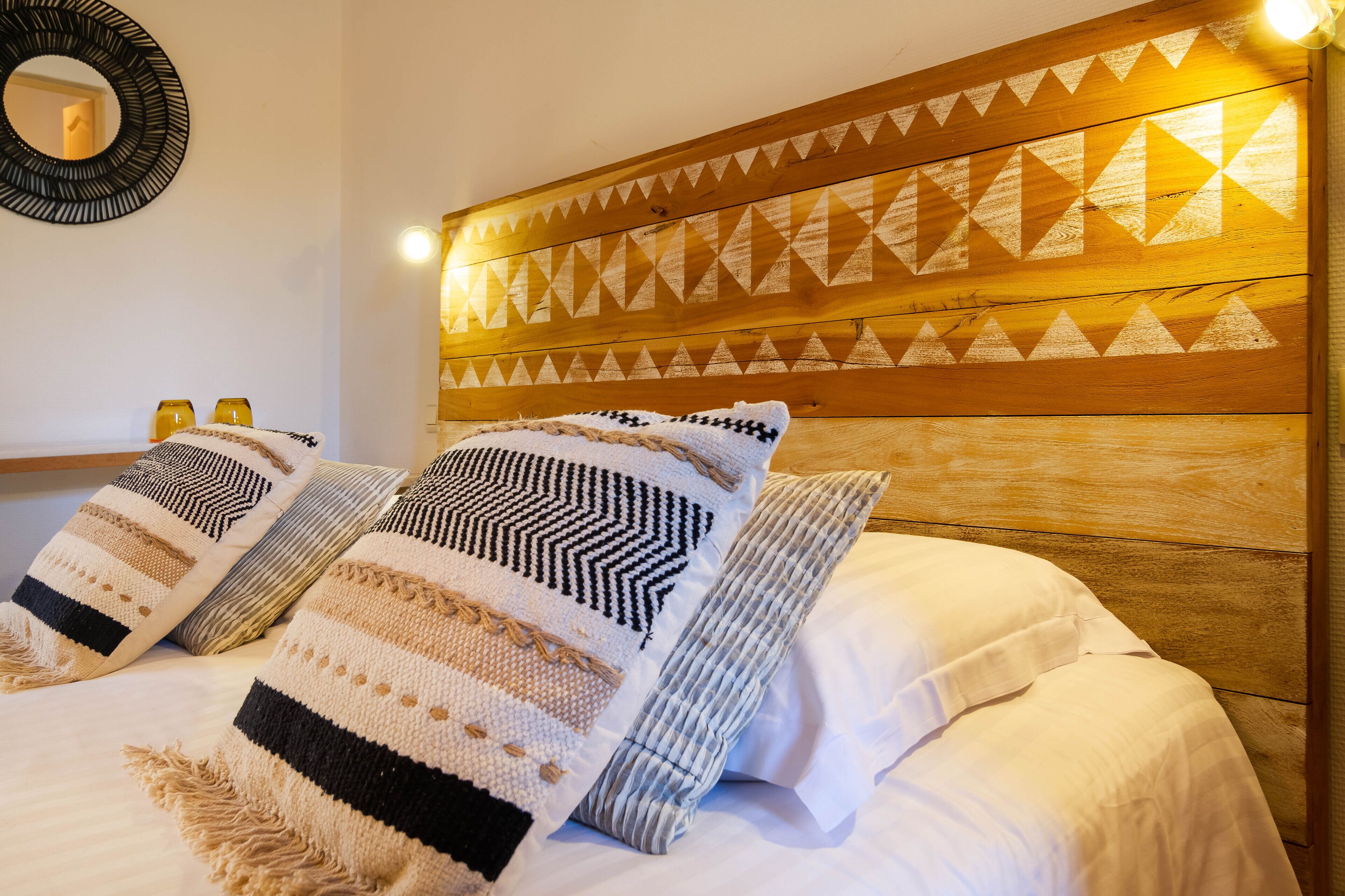 A bed with patterned pillows and a wooden headboard with geometric designs.