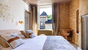 Un dormitorio con una cama grande, una ventana con cortinas, una silla de mimbre y una pared de piedra.