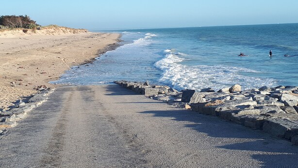 Una playa arenosa con un rompeolas rocoso y mar tranquilo.