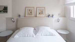 Ein Hotelzimmer mit einem Bett, zwei Wandlampen, einem kleinen Tisch und zwei gerahmten Kunstwerken an der Wand.