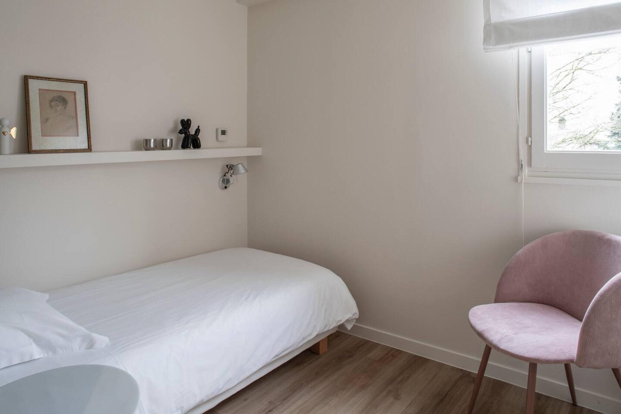 Une petite chambre à coucher, bien rangée, avec un lit simple, une chaise et une étagère où sont posés des objets personnels.