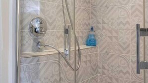 Eine Dusche mit Glastür, Duschbrausehandstück und einer Seifenspender auf einem Regal.