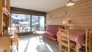 Une pièce avec un intérieur en bois, un canapé, une table avec des chaises et une grande fenêtre donnant sur les bâtiments à l’extérieur.