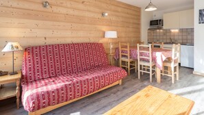 Een gezellige kamer met een houten bank, een eettafel met stoelen, een lamp en een keukenhoek met kastjes en een magnetron.