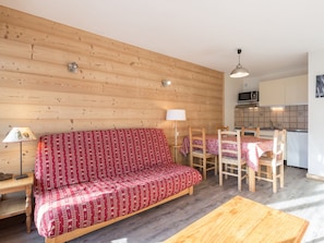 Una habitación acogedora con un sofá de madera, una mesa de comedor con sillas, una lámpara y una zona de cocina con armarios y un microondas.