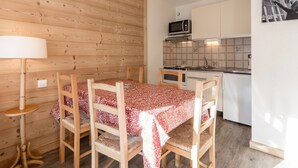 Een compacte keuken met een magnetron, fornuis en spoelbak. Er is een eettafel met stoelen en een lamp. De kamer heeft houten lambrisering.
