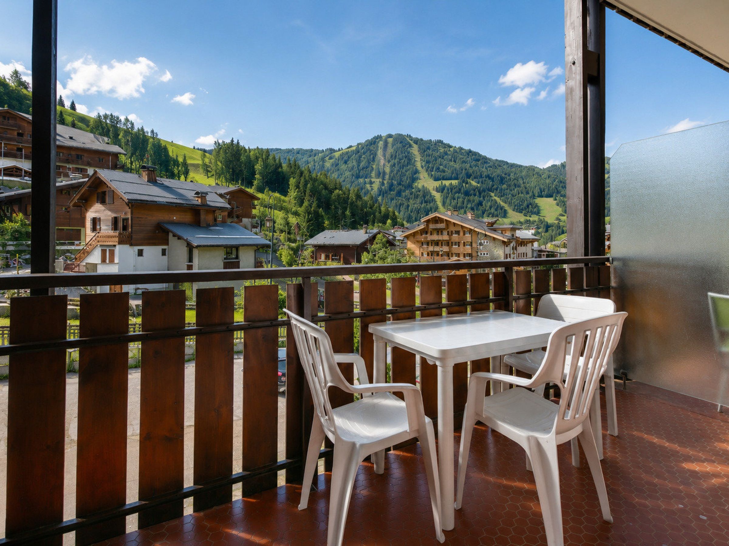 Un balcón con mesa y sillas, con vista a un paisaje montañoso con edificios.